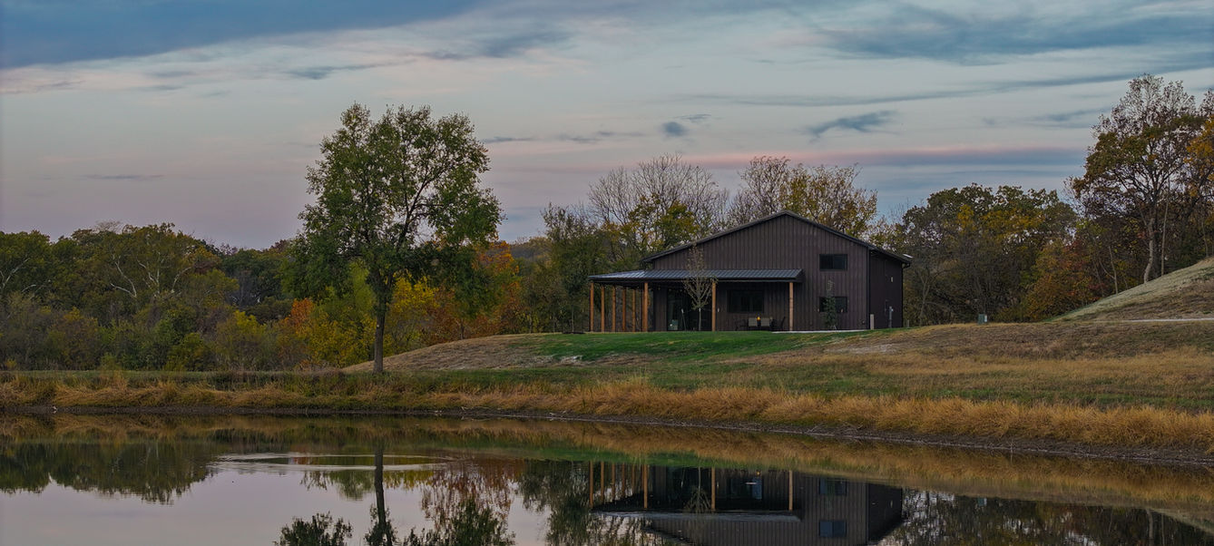 Wide angle shot of a barndominium on the right with lake in foreground.