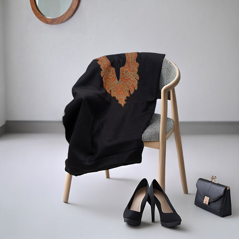 Black dress with intricate orange embroidery draped on chair, paired with black heels and handbag on white floor, mirror on wall.