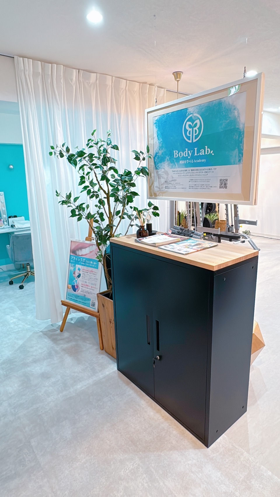 白いカーテンと観葉植物のある明るい店内。黒い受付台に「Body Lab.」の看板が掲げられ、清潔で落ち着いた雰囲気。