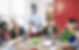 Professor sorridente conduzindo uma aula com alunos em uma mesa, interagindo e estudando juntos.