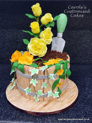 Gardening celebration cake with handmade sugar paste flowers and plants and trowel in a wooden tub.