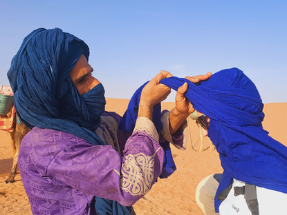 nomade du désert marocain qui aide une voyageuse à mettre un chèche traditionnel