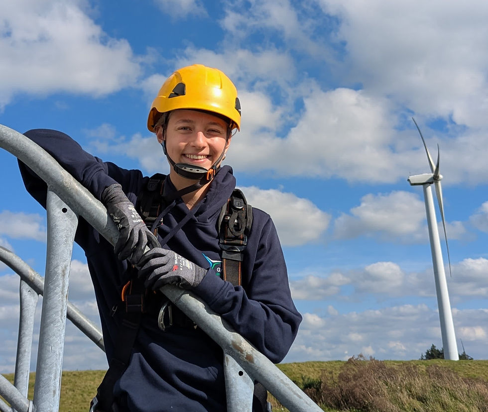 Smiling person in yellow helmet at wind turbine; blue sky with clouds.