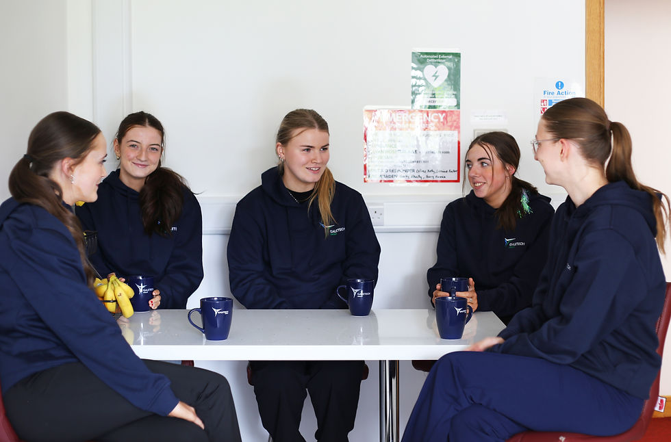 Group of girls in navy hoodies sit around a white table chatting.
