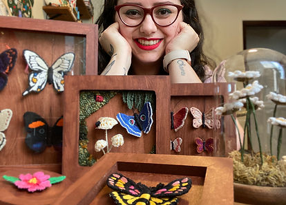 foto com peças de bordados em molduras de madeira e redoma de vidro