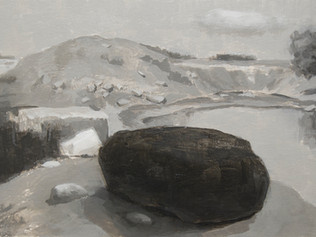 Large black rock and small white rock with a view of a rock quarry. Body of water to the right.