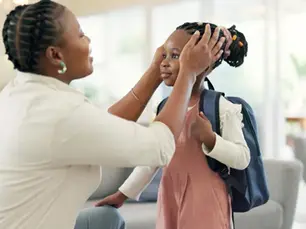 Getting ready morning and a mother with a child for school leaving kiss and talking in the living room happy speaking and an african mom helping a girl with a backpack in a house for kindergarten