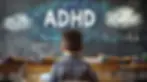 Child in plaid shirt sits at a desk in a classroom. "ADHD" is written on the blackboard with colorful chalk clouds. Classroom setting.