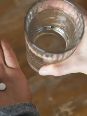 A person holds a glass of water and a few pills, highlighting the struggle and complexity of substance abuse.