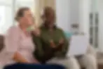 Senior multiracial couple discussing over laptop while sitting on sofa at home. unaltered,
