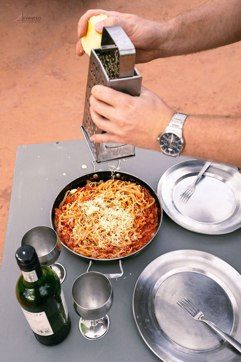 Hands grating cheese over spaghetti outdoors