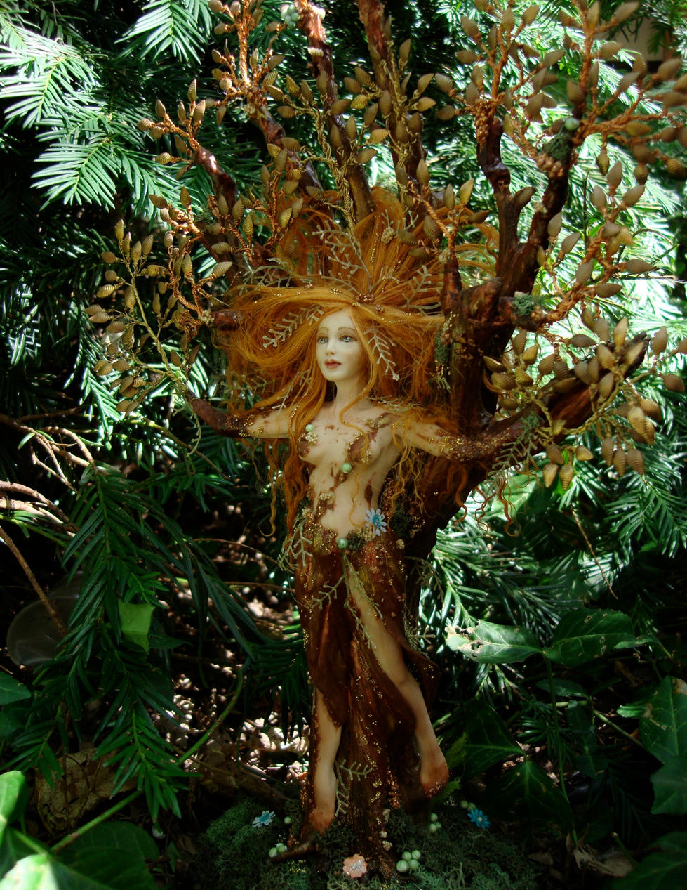 a red-haired dryad steps from her tree trunk, branches fanned over her head, hair fanned out into them.