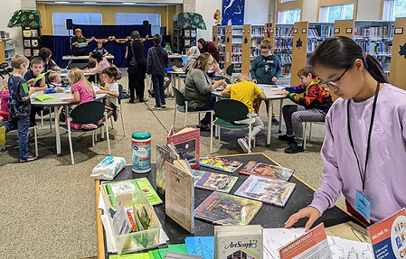 Children making art at tables while another child explores books on a table