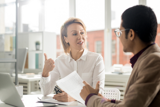 Manager and employee discussing a document across a desk in a bright office.