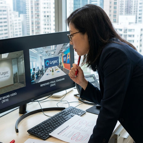 香港形象影片更新時機評估 — 行銷總監在辦公室螢幕前並排對比現有品牌形象影片畫面與最新品牌視覺標準,評估形象影片更新必要性