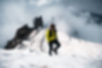 Wanderer in gelber Jacke auf einem verschneiten Berggipfel