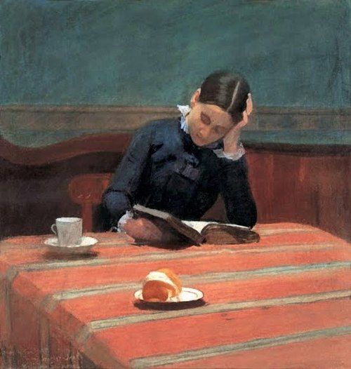 A girl reading at a café table with coffee and bread, resting her head on her hand
