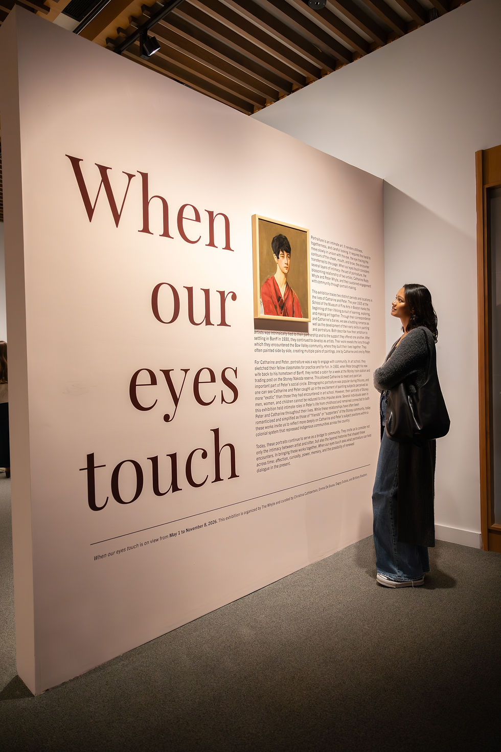 Woman in a museum gallery reads an exhibit wall titled When our eyes touch beside a portrait.