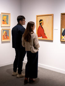 Two visitors view framed portraits in a gallery at The Whyte featuring When our eyes touch exhibition, with white walls and gray carpet.