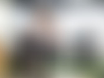 Woman with crutches and leg brace stands in a rehab centre as a therapist assists. Exercise equipment, grey walls, and a calm atmosphere.