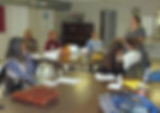 woman standing at front of class speaking to participants sitting around a table.
