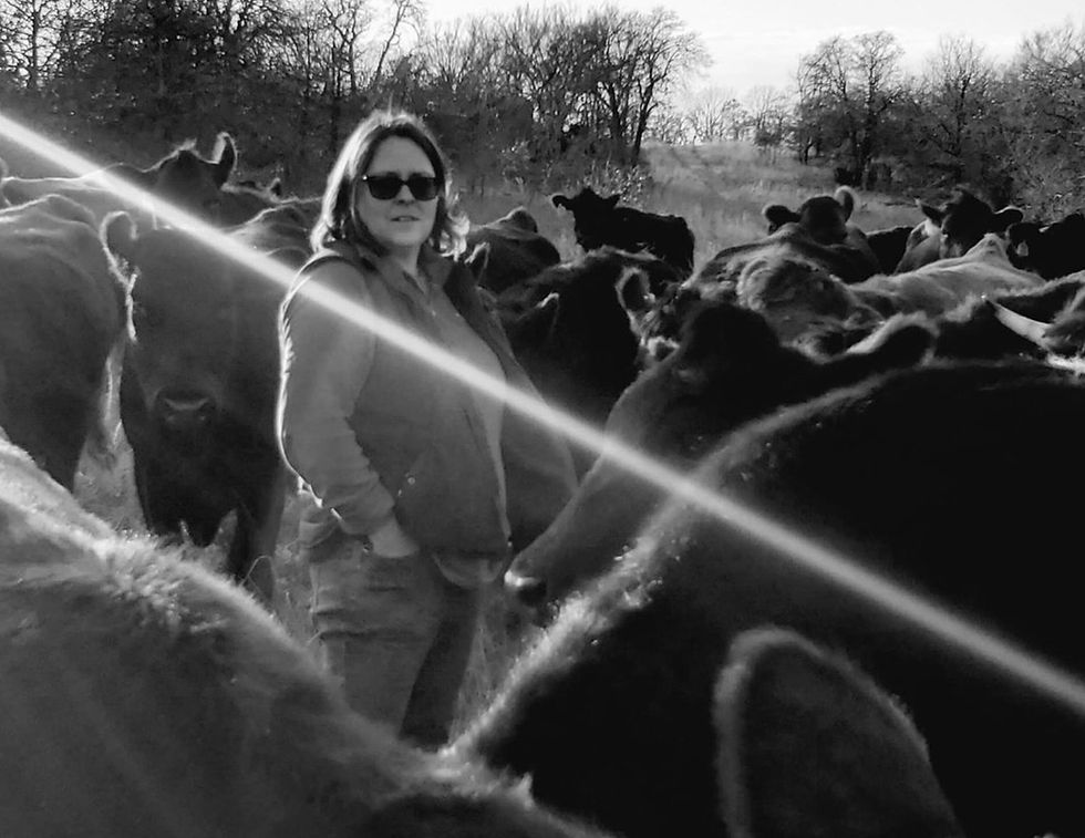 woman with sunglasses standing in field surrounded by cows