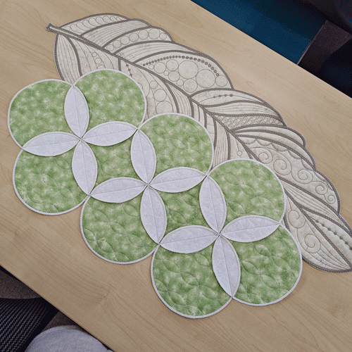 green and white table runner shown with brown & cream feather-shaped embroidered runner