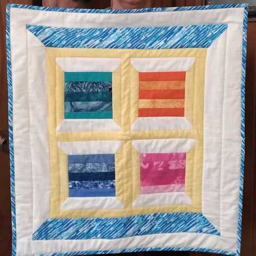 Sandy's first quilt, a wallhanging of colourful set of spools-in-spools