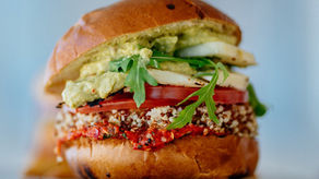 A picture of a vegan burger filled with guacamole, tomatoes, arugula, vegan cheese, roasted tomatoes, and a grain burger. 