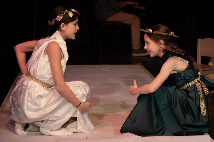Két jelmezes lány játszik a színpadon, egyik hüvelykujjal felfelé mutat.
