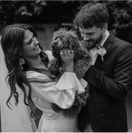 Black and white image of a smiling bride and groom with their toy cavoodle Sadie
