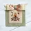 Thumbnail: Bee cross stitch pattern with a beehive on a pedestal, simple flowers, and bees. Their path is stitched, forming a border.
