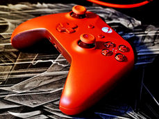 Red gaming controller on a dark, patterned background. The illuminated button glows blue, creating a vibrant contrast.