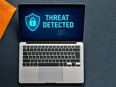 Laptop on a dark surface with "Threat Detected" text on screen, signifying a cyber alert. Orange folder seen on the left.
