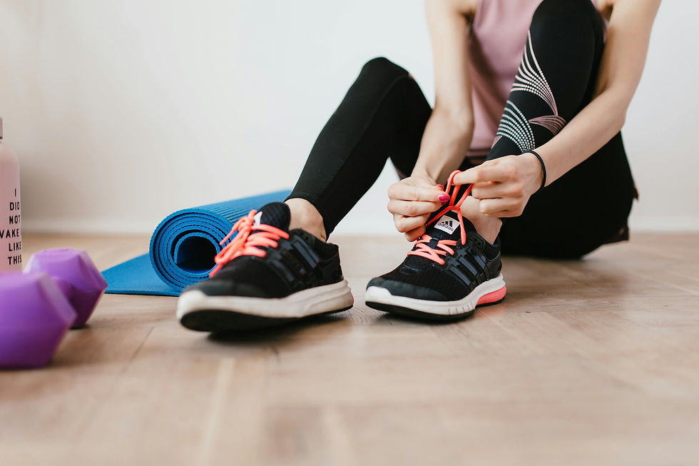 woman tying her shoes next to a yoga mat and weights