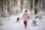 back of a woman walking with her dog through the snowy woods