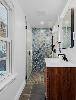 Completed Quincy full bathroom with a glass shower, blue scallop tile, wood vanity, and exterior window.