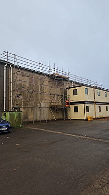 Two-story portable building next to a large industrial warehouse with scaffolding.