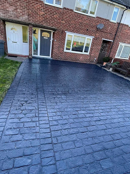 A freshly paved driveway with a dark, sleek finish leads up to a brick row of houses.