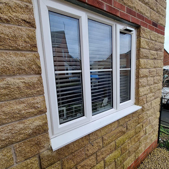A white-framed window with glass panes and horizontal blinds is set in a brick wall