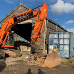 An orange excavator parked in front of a worn wooden barn