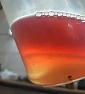 A liquid in a clear measuring cup shows layers of red oil and yellow water