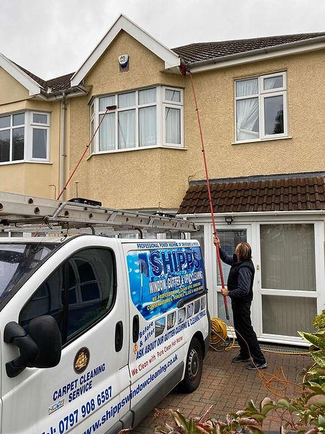 A worker cleans second-story windows of a beige house using an extended pole