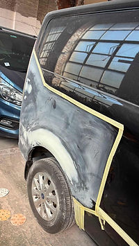 A black vehicle undergoing body repair with sanded primer on the rear quarter panel