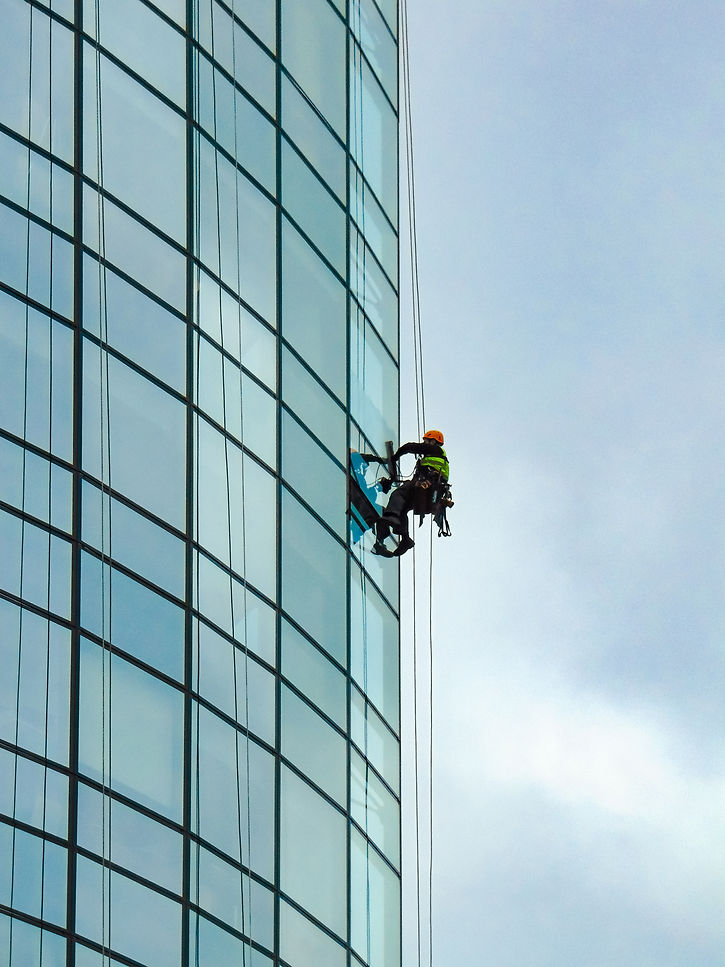 worker secured with harness is cleaning windows of a commercial building