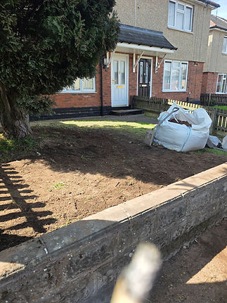 Front yard with freshly tilled soil, bordered by a low brick wall.