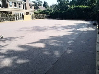 Sunlit outdoor sports court with shadows of trees, surrounded by green hedges