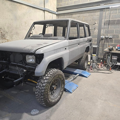 An unfinished SUV with rugged tires sits on a lift in a workshop