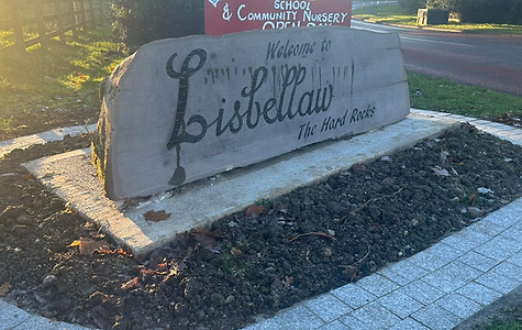 Stone sign reading "Welcome to Lisbellaw, The Hard Rocks" in a landscaped setting