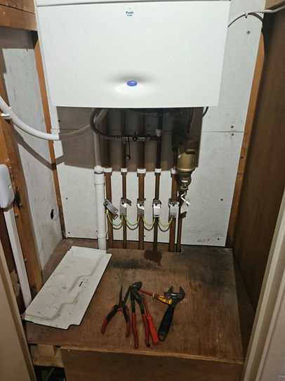 A compact boiler installation in a wooden cabinet with visible pipes